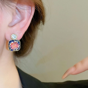 Close-up of pink gemstone square earring with blue enamel and gold trim on model