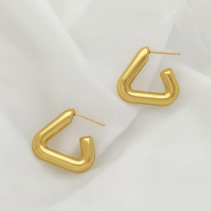 Detailed close-up of golden triangular hoop earrings on elegant white draped fabric