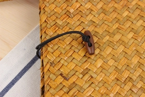 Close-up of woven straw bag detail featuring a natural wooden toggle and elastic closure