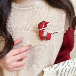 Detail of a red knitted horse brooch pinned to a beige sweater with an artisanal texture