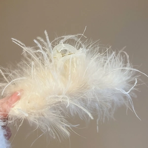 Detail of cream acrylic hair claw clip with plush feathers and crystal embellishments