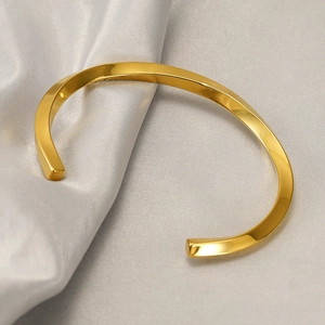 Macro shot of polished gold Mobius twist bangle resting on elegant white silk and marble