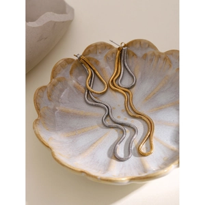 Detail of 18k gold and silver wavy snake chain tassel earrings on a ceramic dish