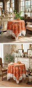 Detail of round orange tablecloth with white floral pattern and delicate lace edges
