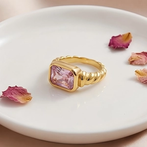 Macro detail of gold twisted band ring with pink rectangular gemstone on white plate