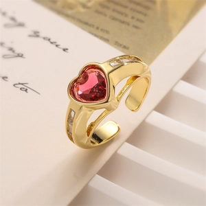 Macro detail of gold open ring with red heart-shaped gemstone on vintage paper