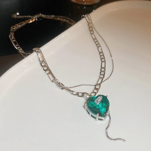 Close-up of double-layered silver necklace featuring a green emerald heart pendant on white plate
