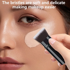 Macro view of soft black and white bristles applying foundation on skin with a black handle