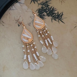 Detail of long tassel drop earrings with white enamel water drops and gold metal chains