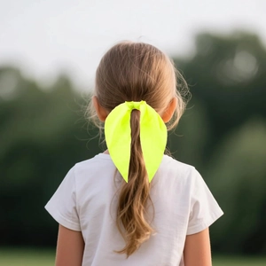 Detail of neon yellow oversized bow hair clip worn by a child in an outdoor setting