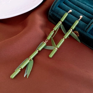 Detailed close-up of green resin bamboo earrings with gold leaves on dark silk fabric