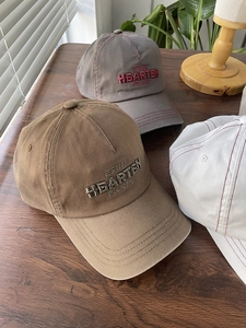 Detail of embroidered letters on cotton baseball caps in brown, grey, and white colors