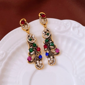 Close-up of vintage gold earrings with colorful crystals on white ceramic plate