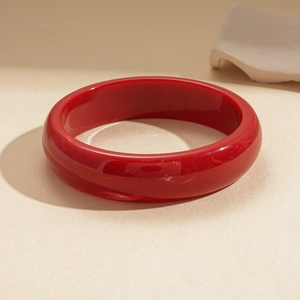 Detailed close-up of glossy red resin round bangle on a textured minimalist background