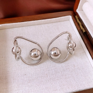 Gros plan de boucles d'oreilles torsadées en métal argenté avec sphère polie sur lin