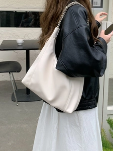 Detail of soft cream leather tote with silver metal chain strap on model's shoulder