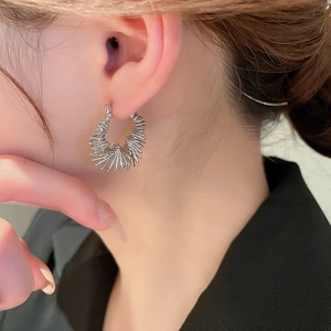 Close-up of silver geometric hoop earring with radial metal texture worn by a model