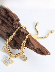 Detail of gold beaded bracelet featuring a butterfly charm with crystals on rustic wood