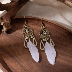Detail of bohemian long feather earrings with white beads on a rustic wooden tray