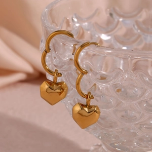 Detail of golden faceted heart pendant earrings hanging on a textured glass rim