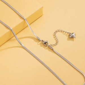 Detail of silver snake chain necklace with heart pendant and extension on yellow box