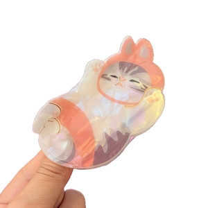 Iridescent cat Griptok with orange bunny hat shown held by fingers on white background