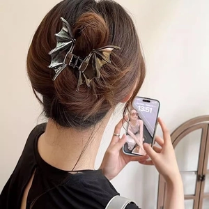 Detail of a metallic bat-shaped hair claw clip worn on a half-up hairstyle by a model