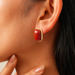 Gros plan d'une boucle d'oreille rétro en résine rouge avec cadre doré sur l'oreille