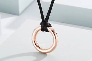 Detailed view of polished rose gold circle pendant on black cord with a soft studio backdrop