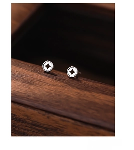 Macro detail of S999 silver coin earrings on dark wood with star-shaped inner cutouts