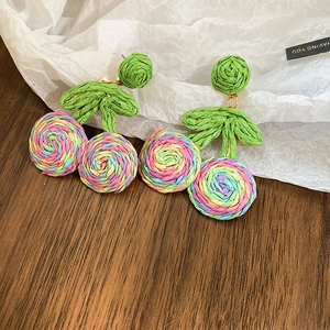 Detailed shot of handmade woven cherry earrings with colorful yarn and green leaves