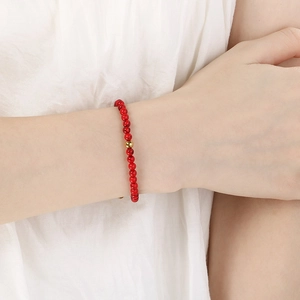 Détail macro d'un bracelet en perles rouges avec perle dorée porté au poignet