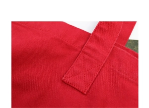 Close-up of red washed canvas bag showing cross-stitched handle detail and fabric texture