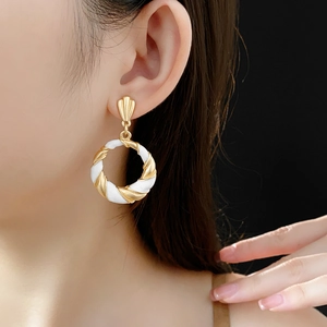 Close-up of vintage twisted gold and white enamel earrings worn on a model with dark background