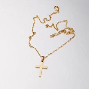 Detailed close-up of a mirror-polished gold cross pendant necklace on gray background