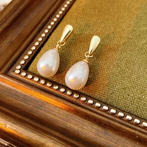 Vintage style drop pearl earrings with golden studs on a textured classic fabric background