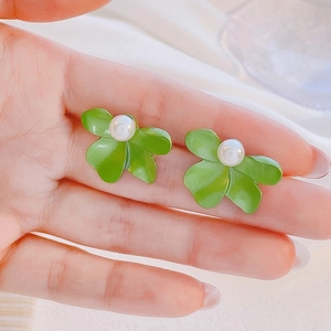 Detailed view of green flower earrings with white pearl center held by hand