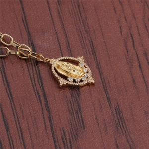 Close-up of golden Virgin Mary pendant necklace with clear zircon stones on dark wood background