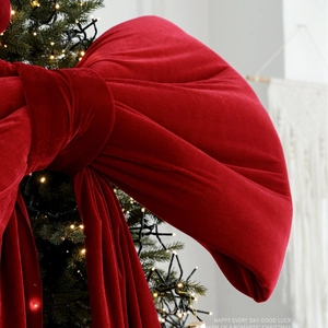 Large burgundy velvet bow topper on a Christmas tree with warm glowing string lights