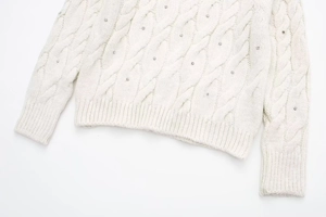 Detailaufnahme von weißem Zopfstrickpullover mit funkelnden Strassstein-Verzierungen