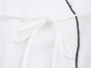 Détail du tailleur en coton et lin blanc avec passepoil noir et taille à nouer ajustée