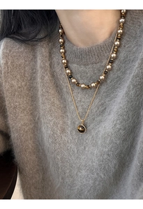 Gros plan d'un collier en œil de tigre doré et perles sur un pull en maille grise