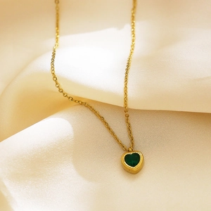 Detail of a gold heart necklace with a green zircon gemstone on smooth cream silk