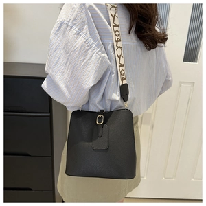 Detail of black pebbled leather bucket bag with jacquard strap worn by a model