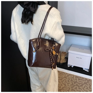 Détail du cabas en cuir verni marron foncé avec nœud tissé et breloque de raquette