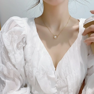 Detail of a gold-plated geometric circle pendant with a white pearl on a model