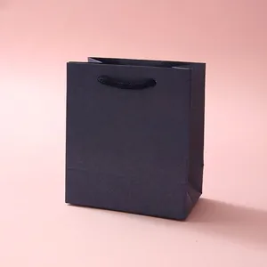 Detailed view of dark grey gift bag with black woven handles on pink background