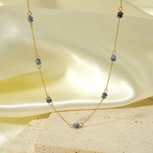 Detail of gold chain necklace with blue natural stone beads over silk and stone background