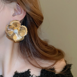 Close-up of oversized gold flower earring with textured petals and center pearl detail