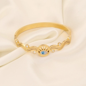 Makro-Detail des goldenen Evil-Eye-Armreifens mit blauem Inlay und Zirkonia auf Satin